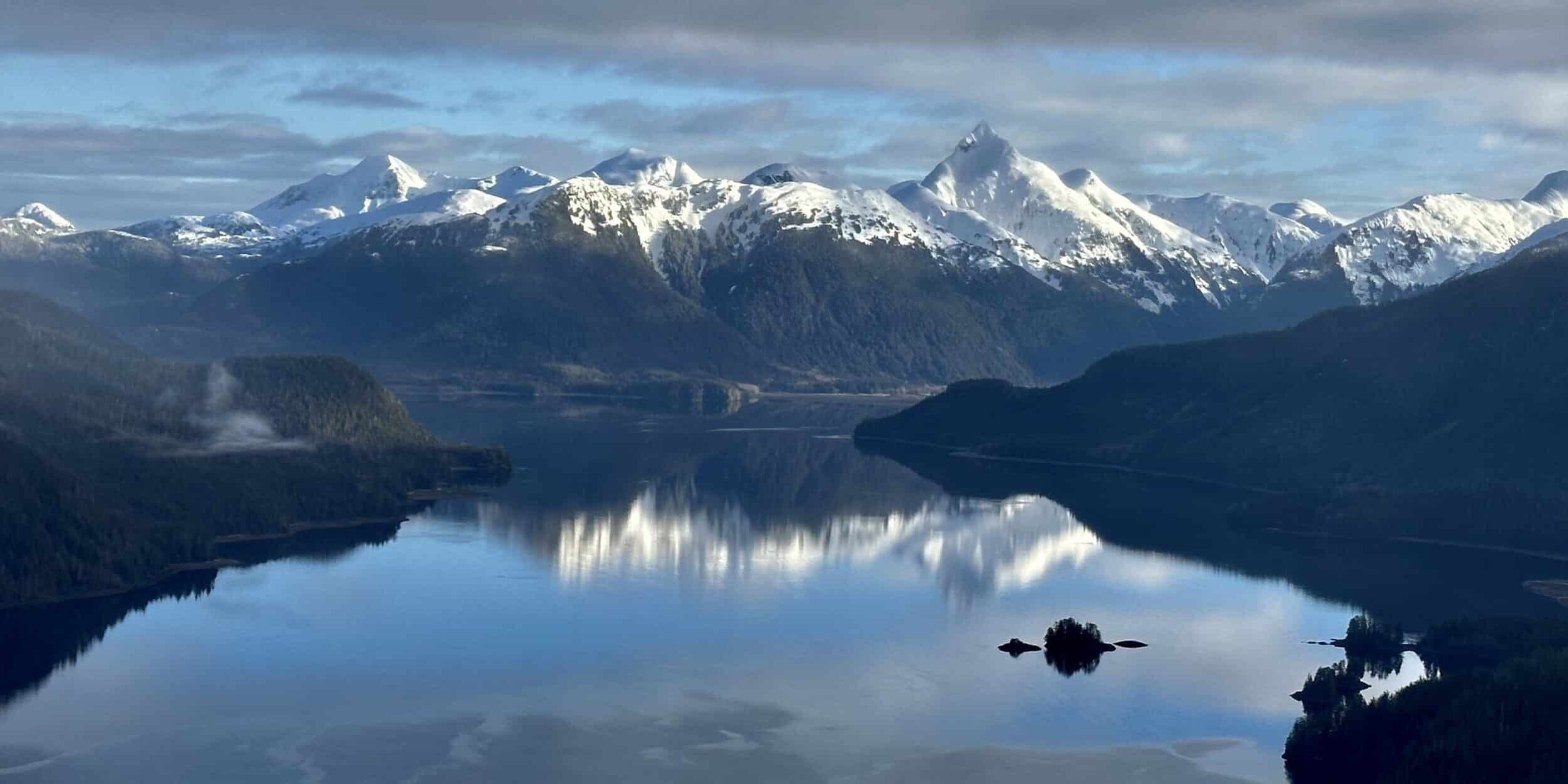 Snow-capped peaks of Southeast Alaska reflected in the still waters of spring — the Inside Passage at its most breathtaking.