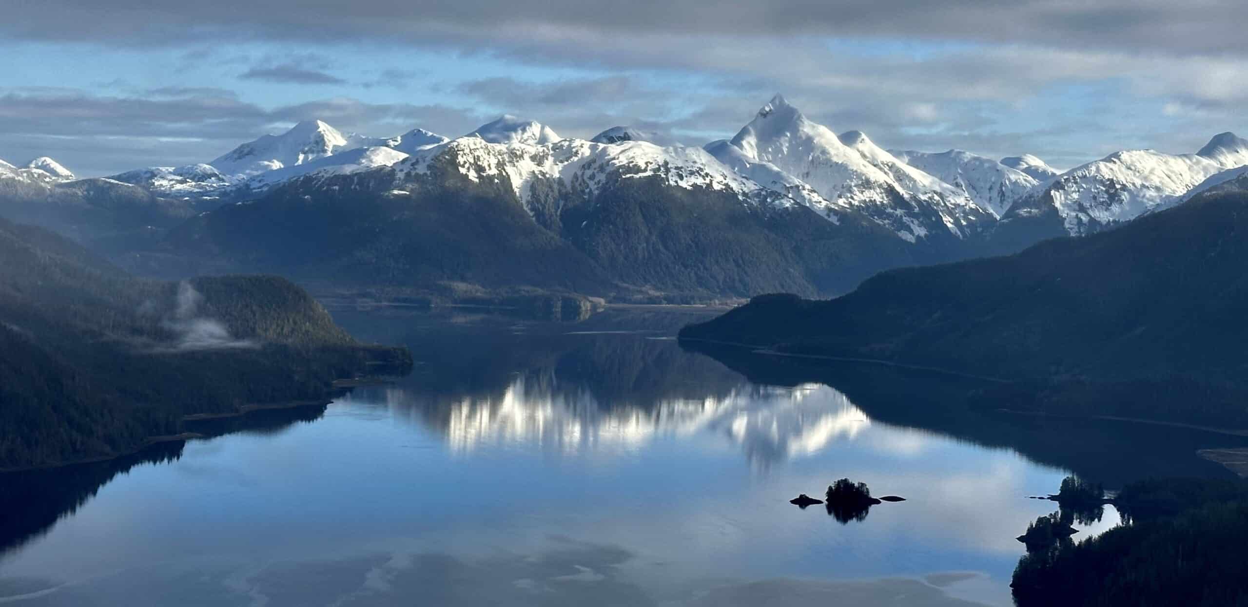 Snow-capped peaks of Southeast Alaska reflected in the still waters of spring — the Inside Passage at its most breathtaking.