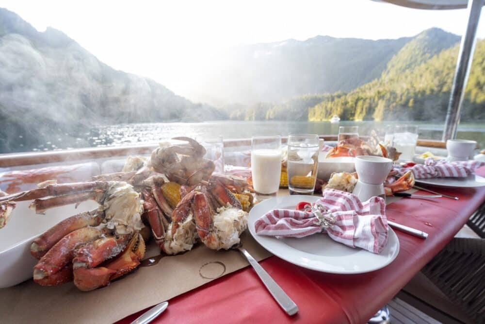 Fresh crab and corn on the deck table of M/Y Dauntless, with a misty Southeast Alaska fjord behind. 