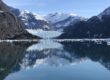The blue face of LeConte Glacier meeting the sea, with snowy peaks reflected in the calm, ice-dotted water of LeConte Bay near Petersburg, Alaska.