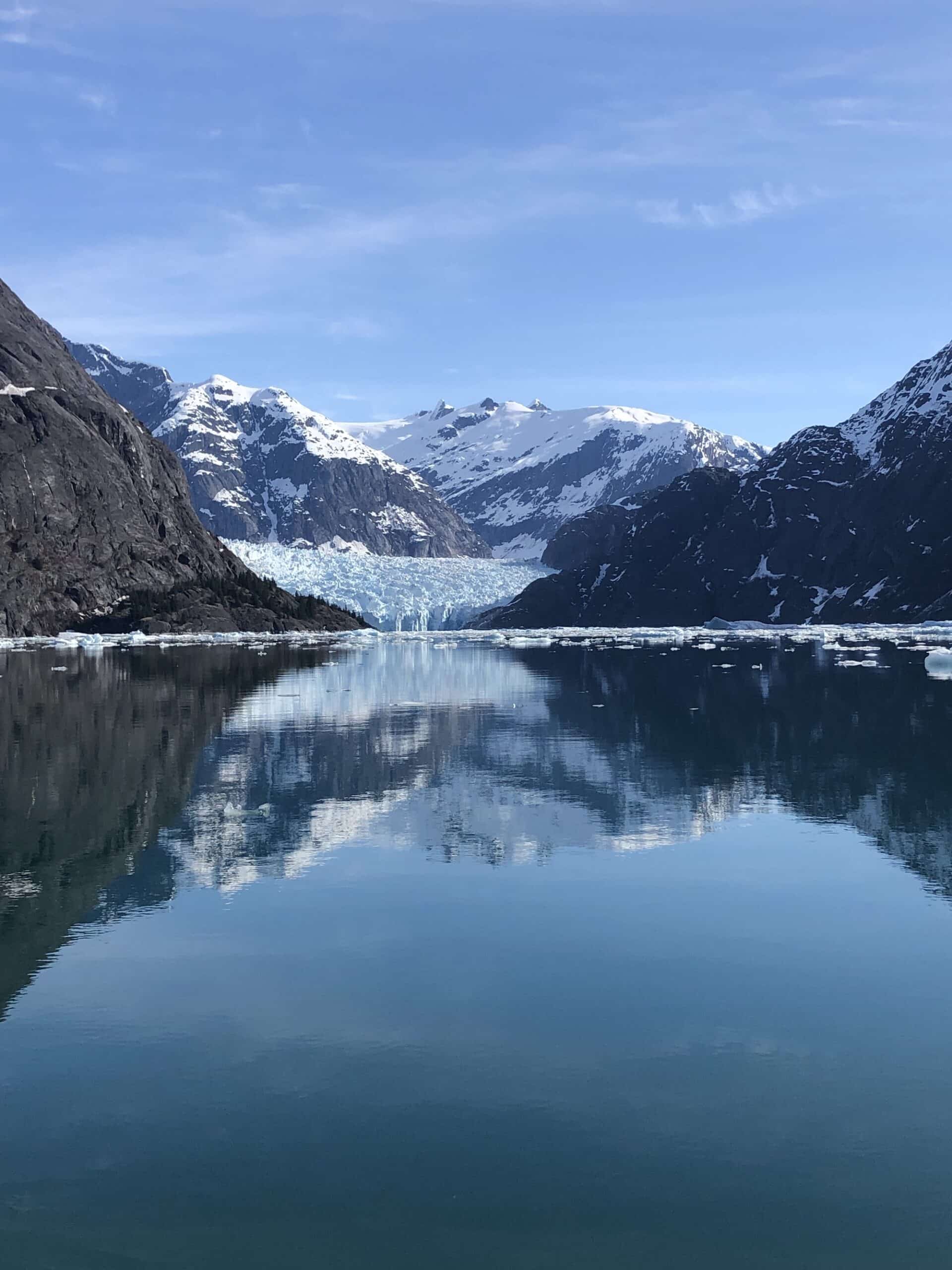 The blue face of LeConte Glacier meeting the sea, with snowy peaks reflected in the calm, ice-dotted water of LeConte Bay near Petersburg, Alaska.