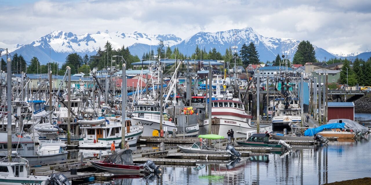 Fishing boats fill the harbor in Petersburg, Alaska, with the town and snow-covered mountains behind.